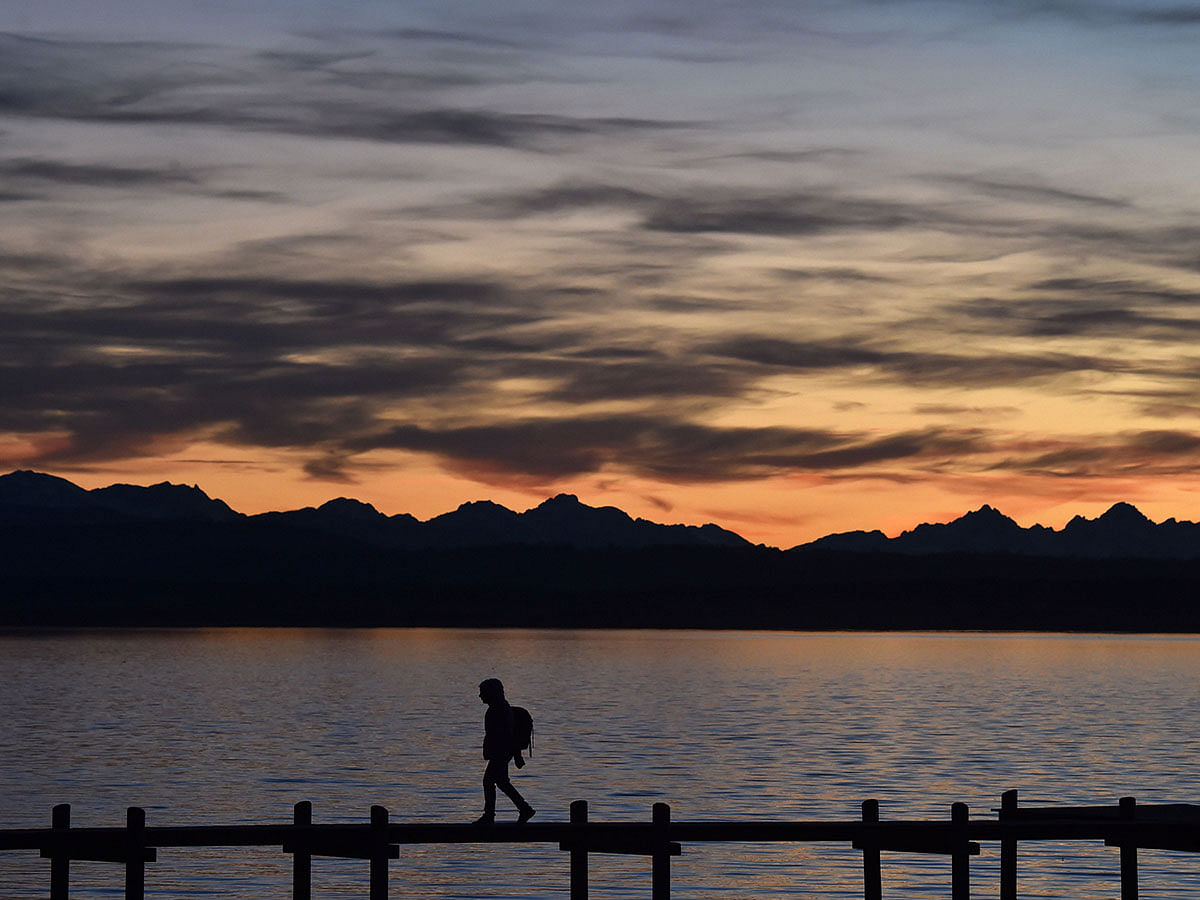 A person walks along a pier in front of the Alp mountainsthe shore of the lake Ammersee in Herrsching, southern Germany, as the sun sets on 9 January 2020. Photo: AFP