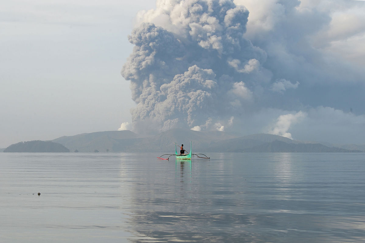 A youth living at the foot of Taal volcano rides an outrigger canoe while the volcano spews ash as seen from Tanauan town in Batangas province, south of Manila, on 13 January. Photo: AFP