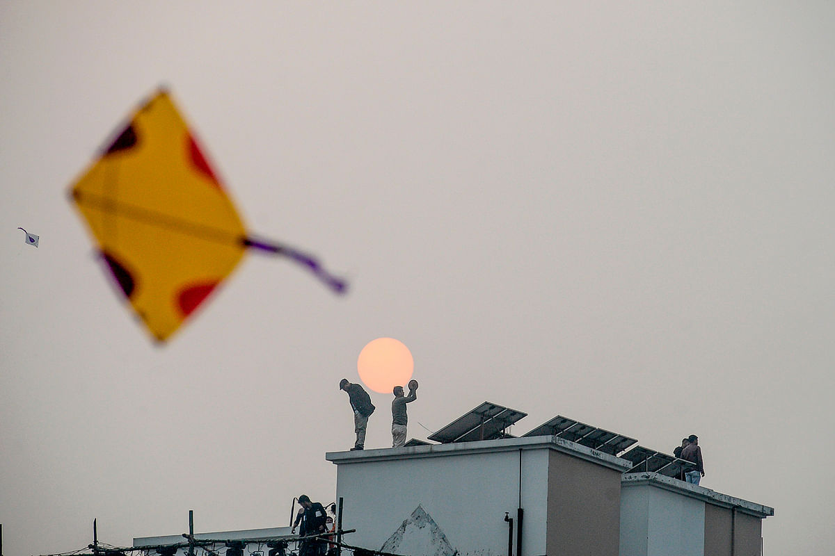A youth flies a kite as others stand on the roofs of houses during the Shakrain festival or the Kite festival in Dhaka on 14 January 2020. Photo: AFP