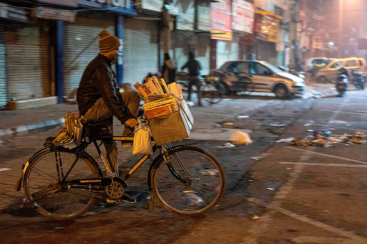 A worker rides a bicycle loaded with newspapers to distribute them early in the morning in New Delhi on 19 January 2020. Photo: AFP
