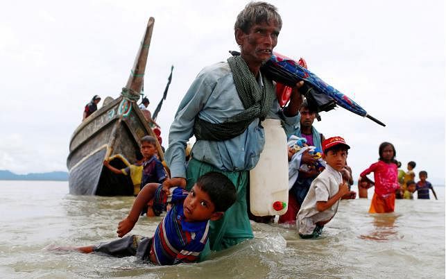 A Rohingya refugee man pulls a child as they walk to the shore after crossing the Bangladesh-Myanmar border by boat through the Bay of Bengal in Shah Porir Dwip, Bangladesh, on 10 September 2017. Photo: Reuters