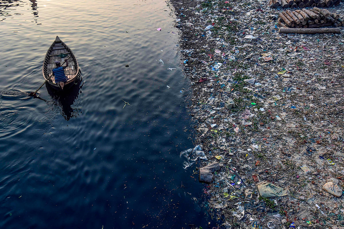 A man paddles on a boat as plastic bags float on the water surface of the Buriganga river in Dhaka on 21 January 2020. Photo: AFP