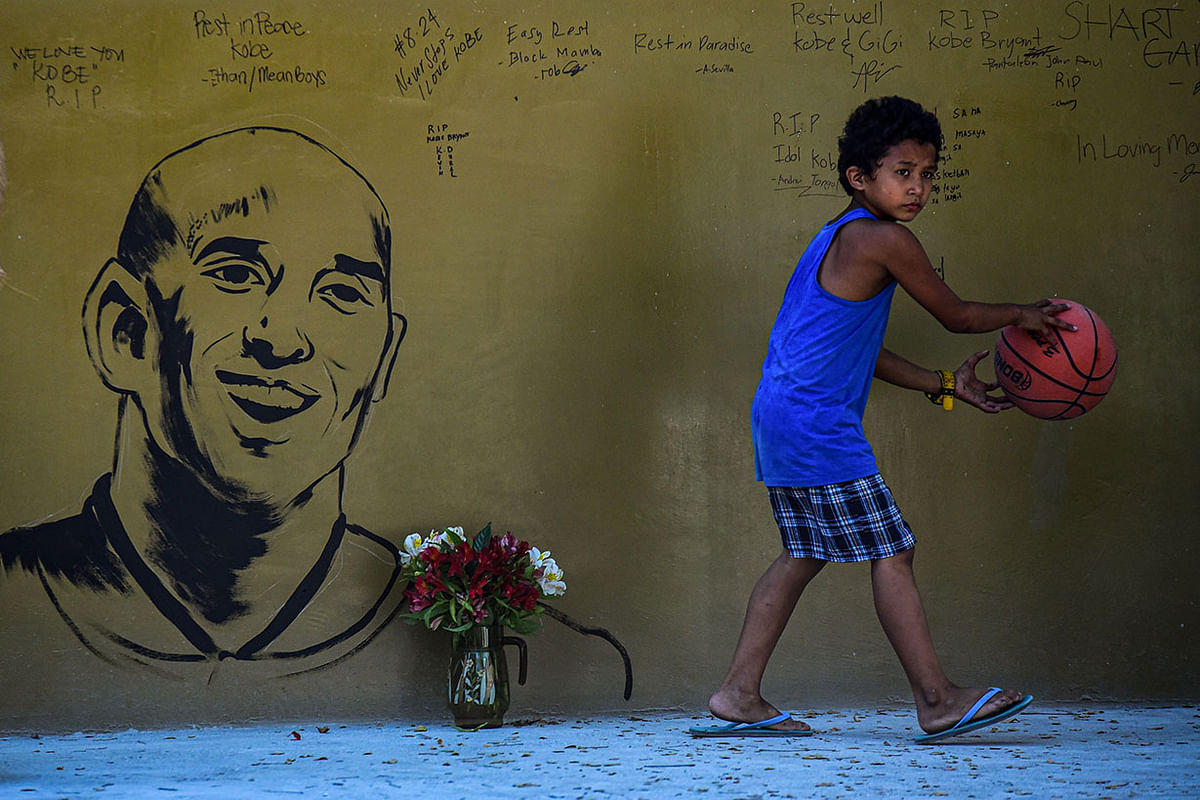 A boy with a basketball walks past a memorial wall for former Los Angeles Lakers basketball player Kobe Bryant following his death overnight in the US, near the `House of Kobe` gym built in honour of his 2016 visit to the Philippines, in Manila on 27 January, 2020. Photo: AFP