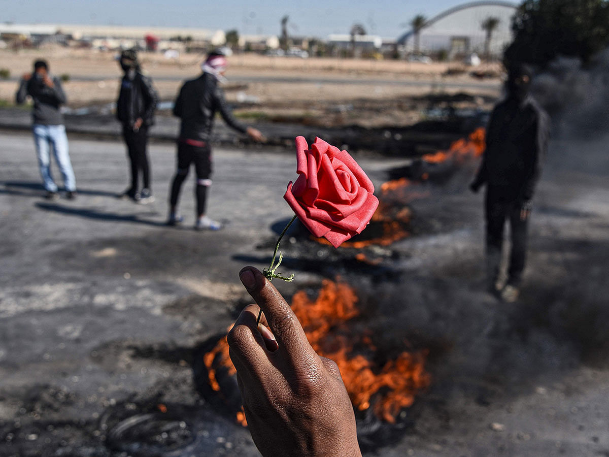 A man holds up a rose before flaming tyres at a make-shift roadblock made by anti-government protesters along the road leading to Najaf International Airport in the central Iraqi holy shrine city on 26 January 2020. Photo: AFP