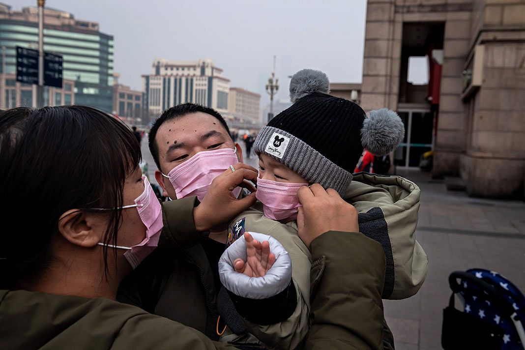 A mother (L) of a child (R) held by his father (C) adjust his protective mask to help stop the spread of a deadly virus which began in Wuhan peaks through a plastic curtain at the Beijing railway station in Beijing on 27 January, 2020. Photo: AFP