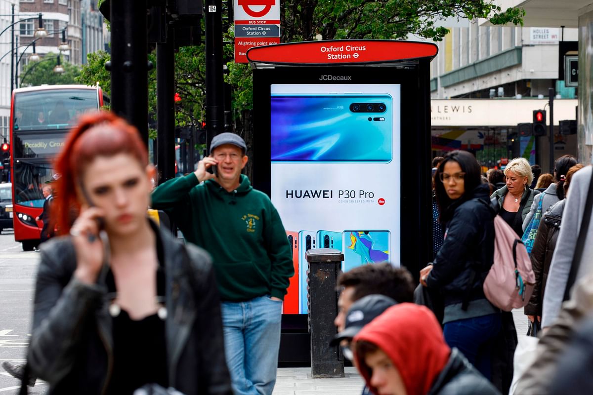 In this file photo taken on 29 April 2019, pedestrians use their mobile phones near a Huawei advert at a bus stop in central London. Photo: AFP