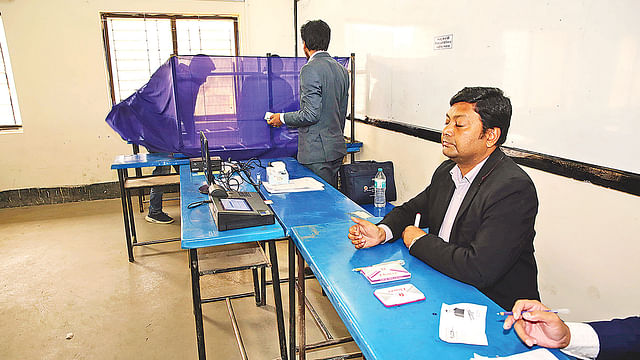 An outsider stands behind a voter in a booth. The voter is being forced to cast his vote in favour of specific candidate at a cente at Dhaka Residential Model College