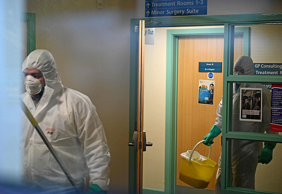 In this photograph taken through a window, workers dressed in protective clothing, including face masks and gloves, are pictured carrying buckets as they work inside of The County Oak Medical Centre in Brighton, southern England on 10 February, 2020, after it closed for `urgent operational health and safety reasons`, following reports a member of staff was infected with the 2019-nCoV strain of the novel coronavirus. Photo: AFP