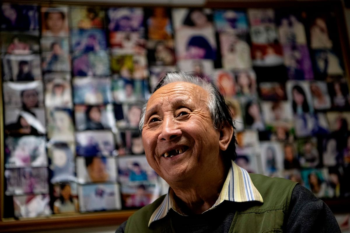This photo taken on 17 December 2019 shows matchmaker Zhu Fang smiling at his house with walls covered with images of single women who have come to him over the years in Beijing. For almost 50 years Zhu Fang has been one of Beijing`s most popular matchmakers, and even now -- aged 75 -- he remains in as much demand as ever. Photo: AFP