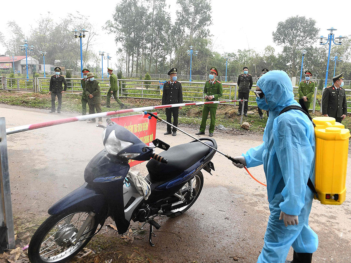 A Vietnamese health official wearing a protective suit amid concerns of the COVID-19 coronavirus outbreak sprays disinfectant on a motorcycle at a checkpoint in Son Loi commune in Vinh Phuc province on 13 February 2020. Photo: AFP