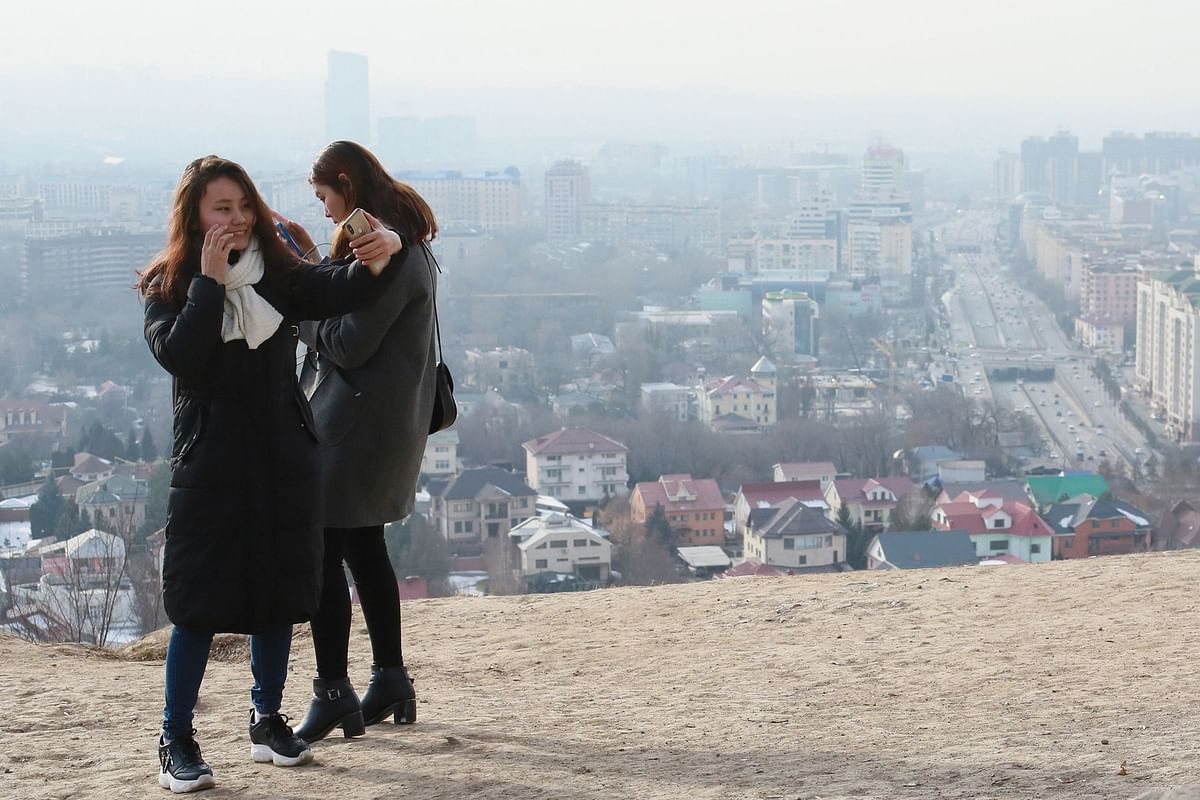 Two young women use their smartphones visiting a viewpoint as smog covers Almaty on 10 January 2020. photo: AFP