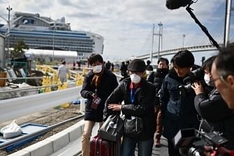 A passenger (C) leaves on foot after dismembarking the Diamond Princess cruise ship (back, L) in quarantine due to fears of the new COVID-19 coronavirus, at the Daikoku Pier Cruise Terminal in Yokohama on 19 February 2020. Relieved passengers began leaving a coronavirus-wracked cruise ship in Japan on 19 February after testing negative for the disease that has now claimed more than 2,000 lives in China. Photo: AFP