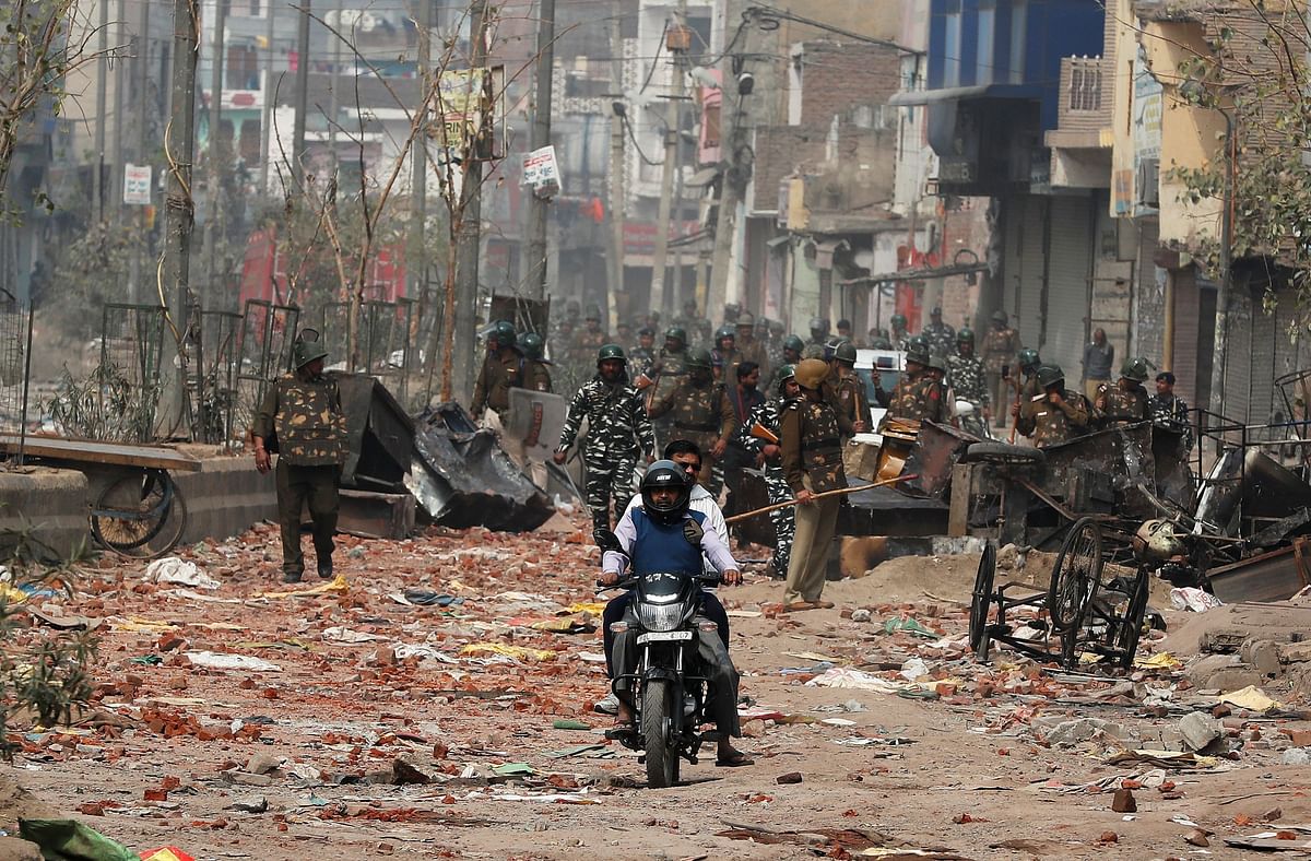 Men ride a motorcycle past security forces patrolling a street in a riot affected area after clashes erupted between people demonstrating for and against a new citizenship law in New Delhi. Photo: Reuters