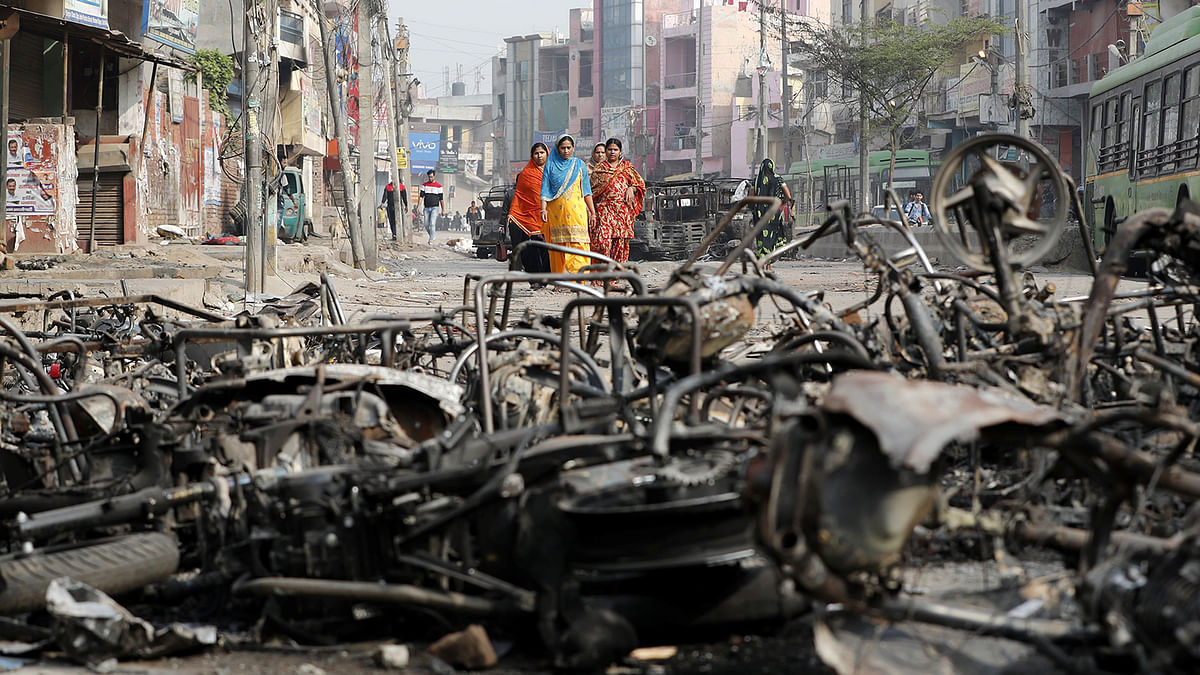 Women walk past charred vehicles in a riot affected area following clashes between people demonstrating for and against a new citizenship law in New Delhi, India, 27 February, 2020. Photo: Reuters